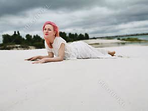 young attractive woman with pink hair in a white dress in boho style on the background of a sandy beach