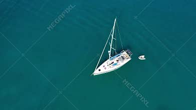 Yacht anchoring in crystal clear turquoise water in front of the tropical island, alternative lifestyle, living on a boat. Aerial