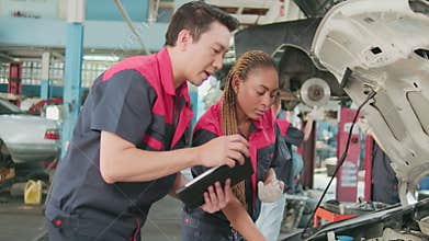 A male automotive supervisor and a Black female mechanic work in a car garage.