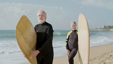 Cheerful elderly surfers standing on shore with surfboards