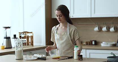 Focused girl in apron whisking eggs and milk in bowl