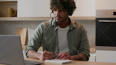 Distant e-learning home education Arabian man in headset watching online computer class laptop webinar at kitchen Indian