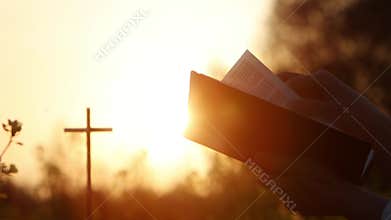 Beautiful sunset light, the cross of Jesus and Christian reading the Bible