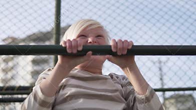 Close-up, slow motion, Blond boy pulling up on the bar on the street.