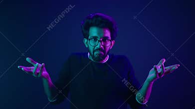 Studio dark blue neon background Indian man Arabian male model guy confused shrug shoulders unsure doubtful