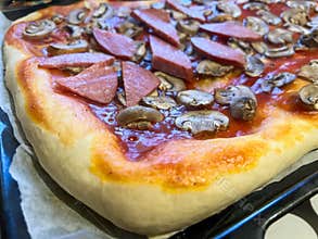 Homemade pizza with mushrooms and sausage resting on baking tray