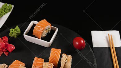 On a stone plate there are sushi rolls with tomatoes and soy sauce.