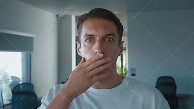 Surprised man lowering glasses in disbelief while working from home, showcasing shock and amazement in his home office