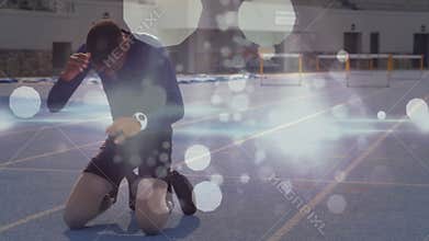 Adolescent male athlete finishing sprint blue track kneeling wiping brow collapsing catching breath