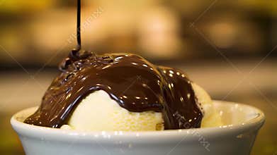 Decadent slow motion pouring of rich chocolate sauce over vanilla ice cream dessert