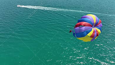 Speedboat pulling a parachute with people moving behind the boat over the water.