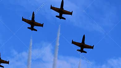 Team aerobatics in formation flight, with jets emitting white smoke trails above the clouds.