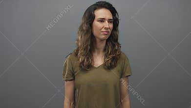 Woman in olive t shirt tilts head while furrowing brow and wrinkling nose in grey studio; skepticism