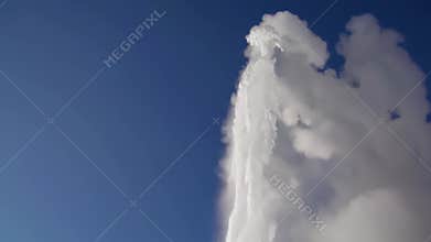 Powerful geyser erupting with billowing white steam against azure sky, showcasing raw geothermal energy rising from
