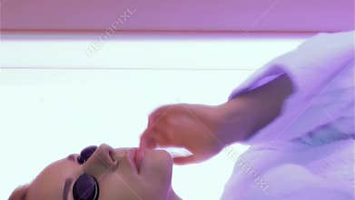 Caucasian woman adjusts goggles in a vibrant tanning booth