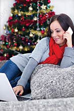 Smiling young woman with laptop sitting near Christmas tree