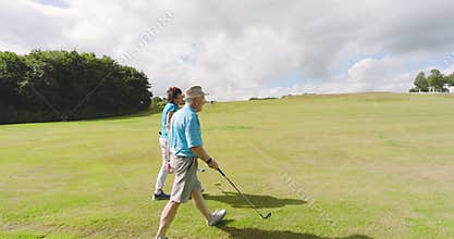Male and female golf players wearing uniforms, talking and walking with clubs on golf course