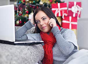 Young woman with laptop sitting near Christmas tree