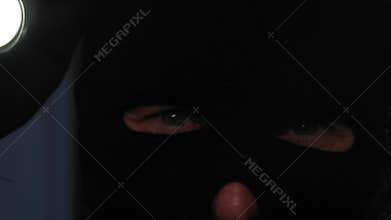 adult man in black balaclava with flashlight illuminates dark room, close-up