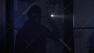 burglary, male burglar in balaclava with flashlight illuminates dark room at night