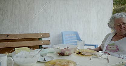 Elderly Woman Wipes Sweat From Brow While Eating Outdoors on Hot Summer Day