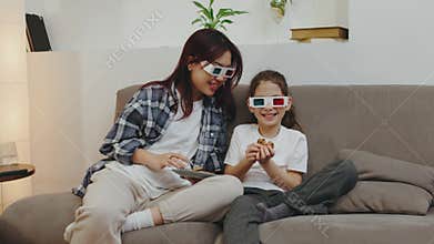 Mom and daughter enjoy a cozy movie night together, wearing 3D glasses, while relaxing on the couch with snacks in a