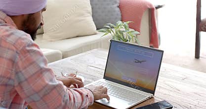 Booking travel online, man using laptop at home with smartphone nearby