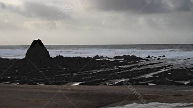 Black rock on Widemouth beach with storm cloud