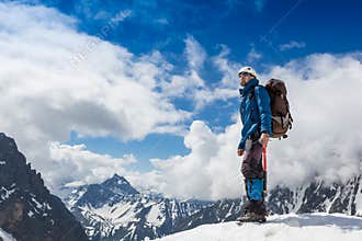 Mountaineer reaches the top of a snowy mountain in a sunny winter day