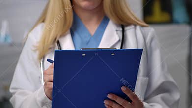 Female Doctor Writing on Blue Clipboard in Hospital Setting