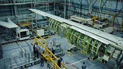 Aircraft assembly facility with engineers and technicians working on the construction of a large airplane wing