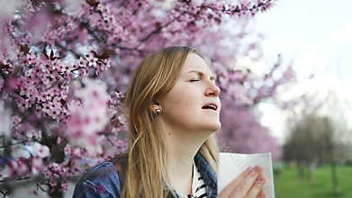 Woman with allergies sneezing under pink cherry blossoms in spring