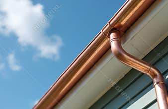 Close-up of copper gutters and downspout. Shiny metal building exterior, residential house with blue sky and clouds.