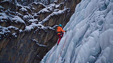 Courageous climber tackles a challenging frozen waterfall, methodically ascending the icy cliff face with specialized equipment