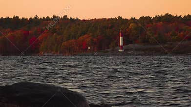 A lake with a lighthouse and a colourful forest in the background during sunset in the fall