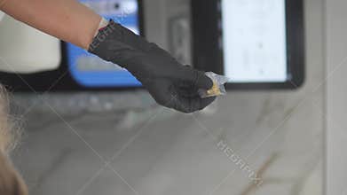 Beautician in black gloves holding a small capsule with golden serum, preparing for a HydraFacial Keravive scalp