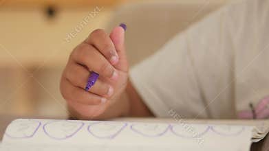 Child drawing with purple crayon on paper