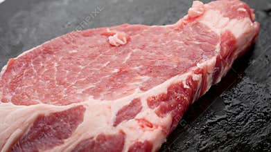 A single, thin pork chop rests on a dark stone slab.