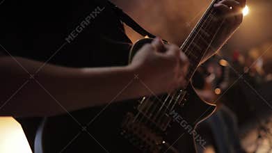 Male guitarist playing electric guitar at concert on stage against yellow light background. Slow motion