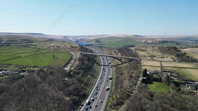 Arched concrete bridge spans across a busy multilane highway running through rolling green hills