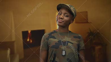 Woman stands smiling in camouflage uniform holding dog tags inside building; confidence service commitment duty