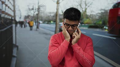 Young man in red sweater talking on phone in a city street with red double-decker buses in the background