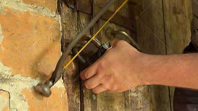Man cutting padlock with hacksaw. Vintage wooden door in brick wall