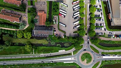 Top view of a busy parking area, restaurants, and roads near a canal in a Dutch town. Buses, cars, cyclists, and a roundabout