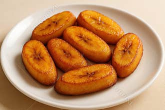 Golden fried plantains arranged on a white ceramic plate, showcasing crispy texture and caramelized surface in warm natural