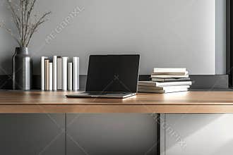 A modern office desk features a laptop open for work, neatly stacked books, and minimalistic decor elements. The sleek