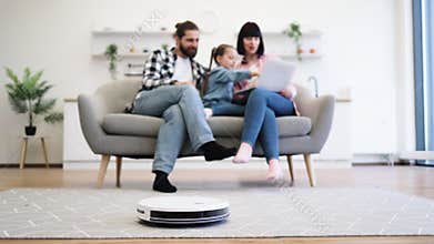 Family relaxing with robot vacuum in modern living room