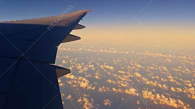 view from the airplane window to the wing and clouds at sunrise, blue sky