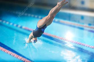 Female swimmer, that jumping into indoor swimming pool.