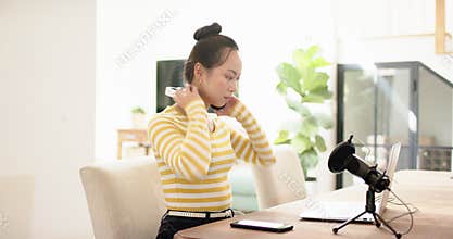 Working and podcasting from home, woman using laptop and microphone, holding headphones